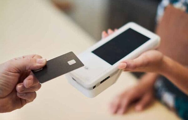 A close-up of a contactless payment being made using a black credit card and a portable card reader.