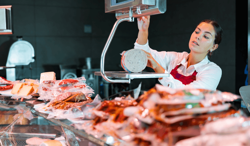 A grocery store worker using a deli scale to slice and weigh meat, showcasing the importance of accurate grocery POS integration for streamlined operations.
