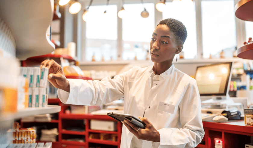 Pharmacist using a tablet to manage inventory on pharmacy shelves